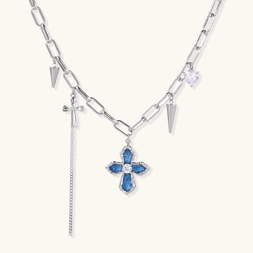 White gold plated chain necklace with blue textured cross pendant, spike charms, and mini cross detail on beige background